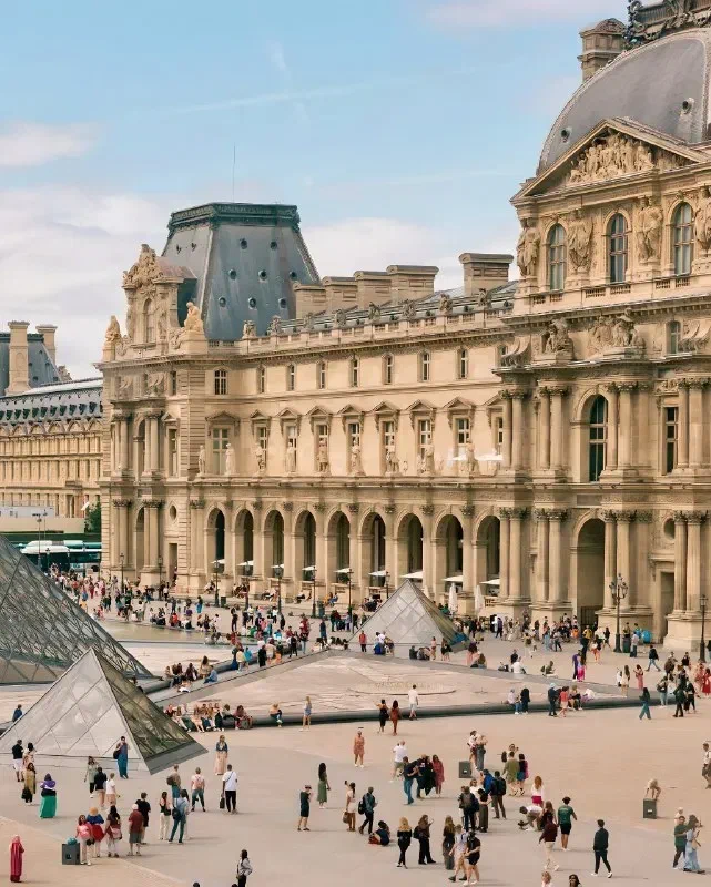 Louvre Palace and visitors in the courtyard, with part of the glass Pyramid at the left.