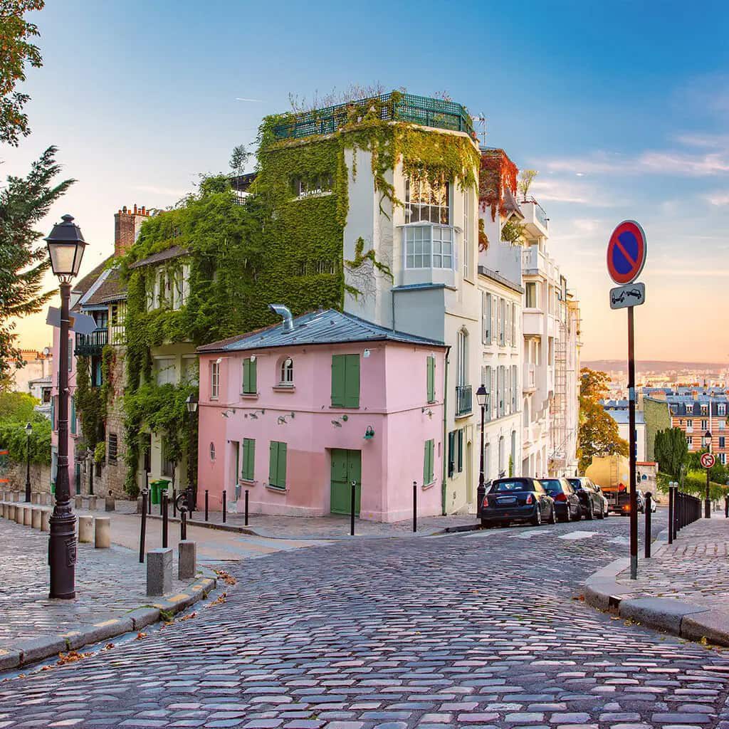 A cobbled Montmartre street beside a pink corner building and ivy-covered façades.