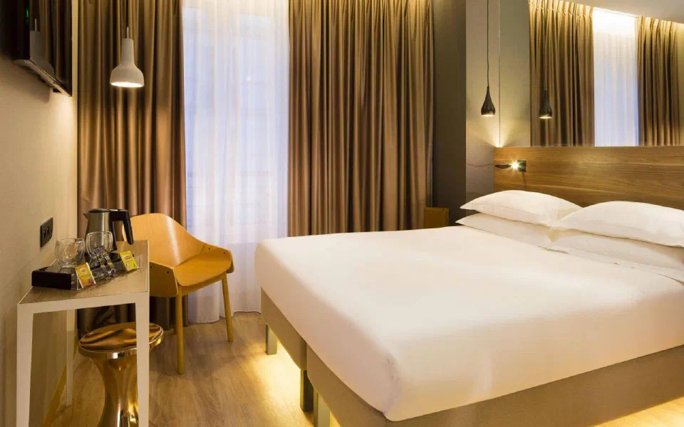 Double room with warm wood finishes and mustard chair at Cler Hotel.