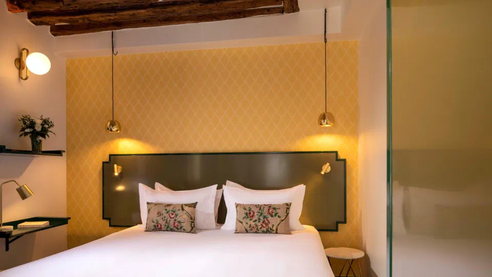 A Charmante room at Hôtel des Deux Îles with a double bed, yellow wallpaper and wooden beams.