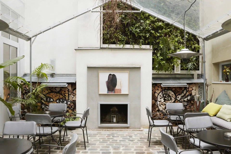 Jules & Jim’s paved courtyard with lounge chairs, a fireplace and a planted wall.
