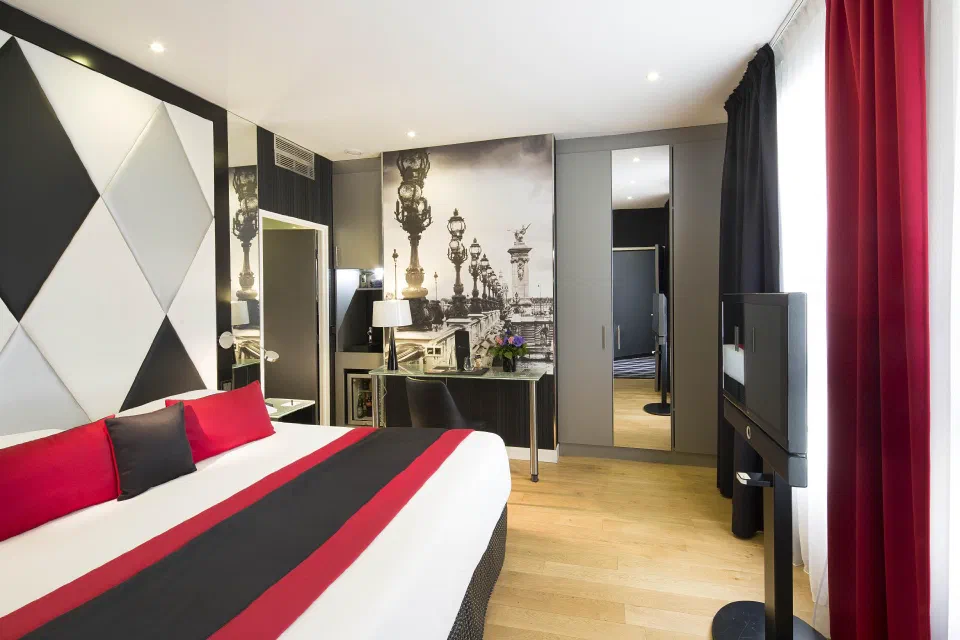 Superior bedroom at L’Empire Paris with red cushions and geometric wallpaper.
