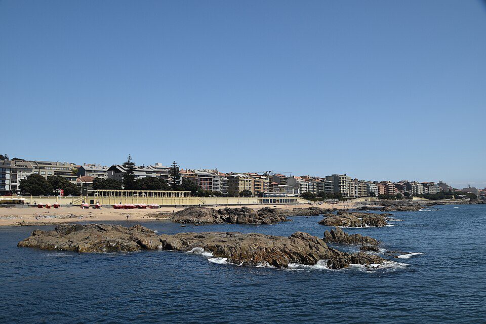 Rocky Atlantic shoreline, sandy beach and promenade on the left, with open sea to the right at Praia do Molhe.