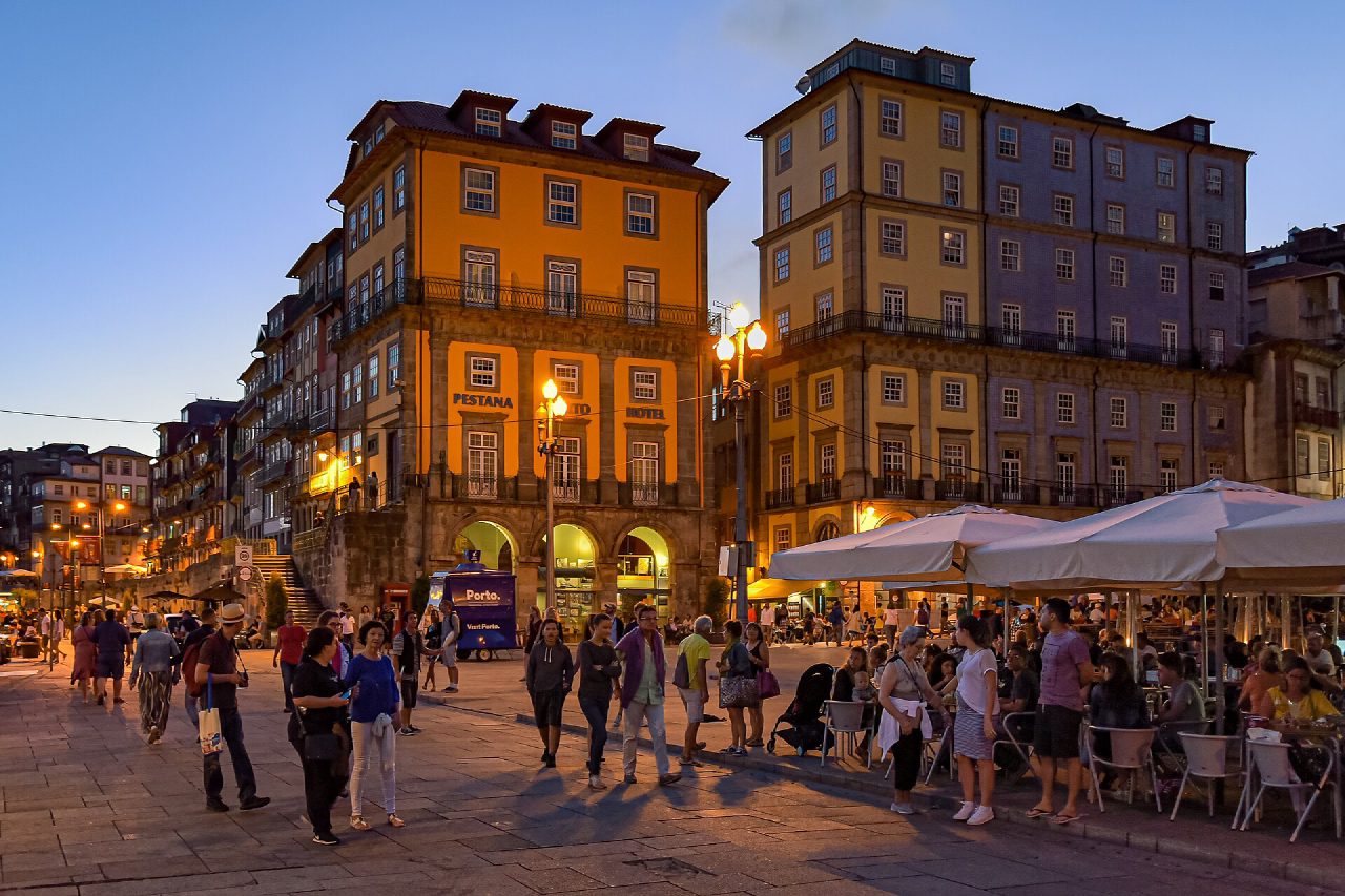 People walking past colourful historic buildings and café terraces in Ribeira at dusk.