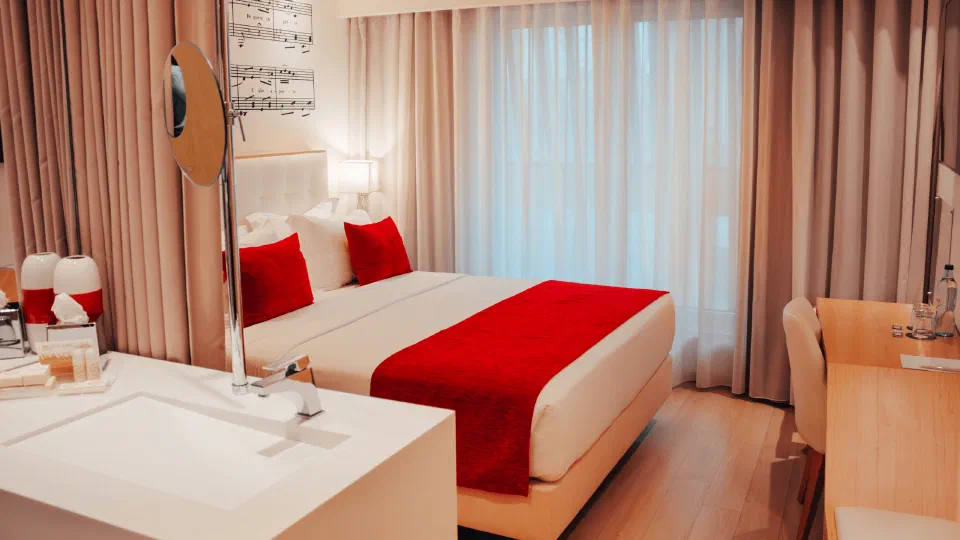 A double bed with a red runner and a musical-score motif on the glass partition at Hotel da Música.