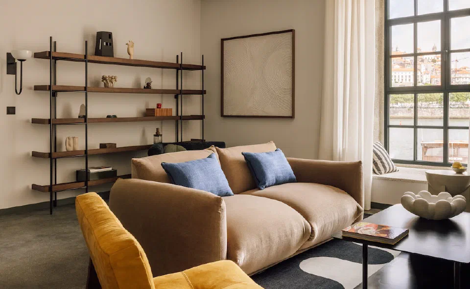 A spacious suite sitting room with a sofa, an ochre armchair and a window looking towards Porto at The Rebello.