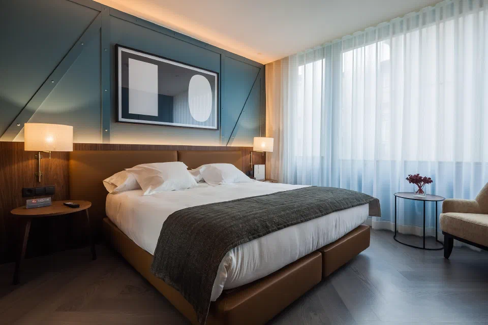 A double bed, geometric wall panels and a window-side chair in a standard room at Vincci Porto.