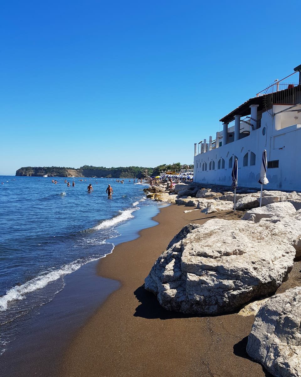 Dark sandy shoreline and waterfront buildings on Procida’s west coast