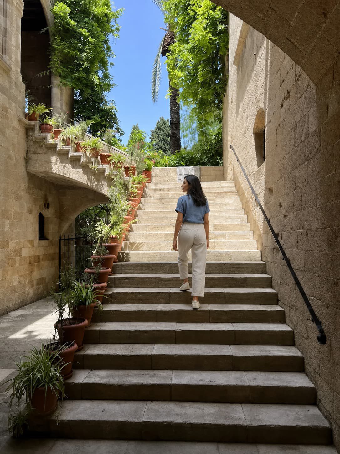A traveller climbing stone steps beside potted plants and medieval walls in Rhodes Old Town.