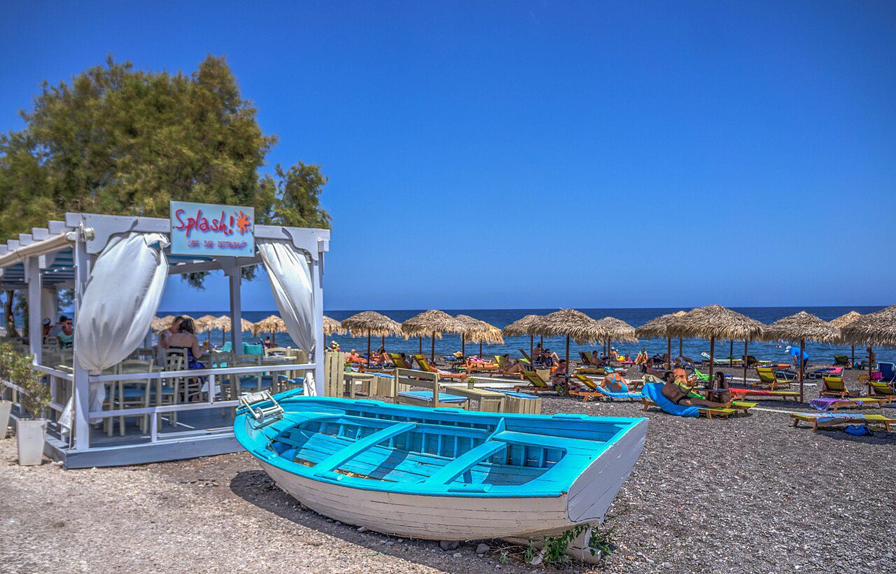 A turquoise boat and parasols on Kamari’s dark-pebble beach.