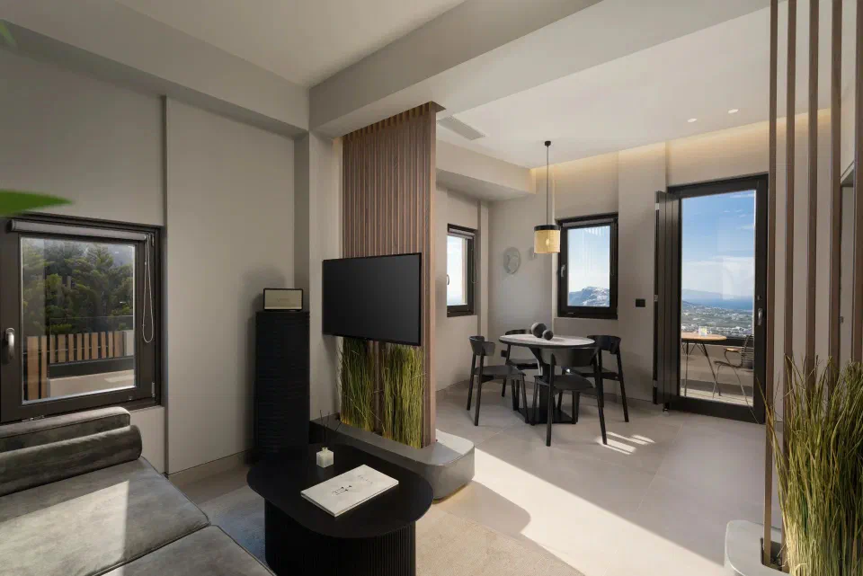 Living and dining area of the Deluxe Suite at Apikia Santorini, with an open terrace door.