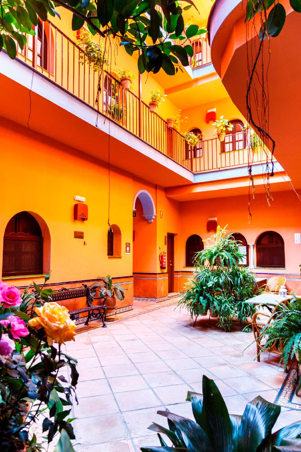 Orange courtyard with tiled floors, leafy plants and gallery balconies at Patio de la Alameda.