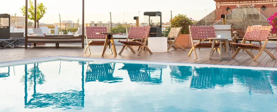 Rooftop swimming pool and timber seating at Zenit Sevilla, with a tiled church roof behind the terrace.