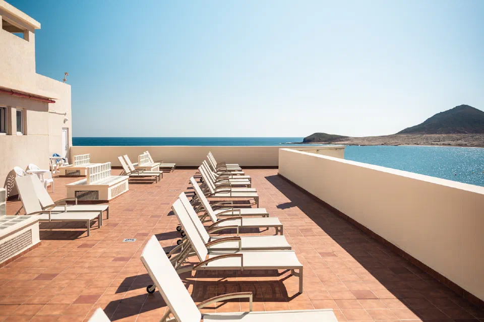 Sun loungers on Hotel Médano’s ocean-facing terrace, with Montaña Roja beyond the bay.