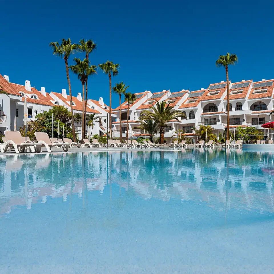 Outdoor pool at Paradise Park framed by palms and white buildings with terracotta roofs.