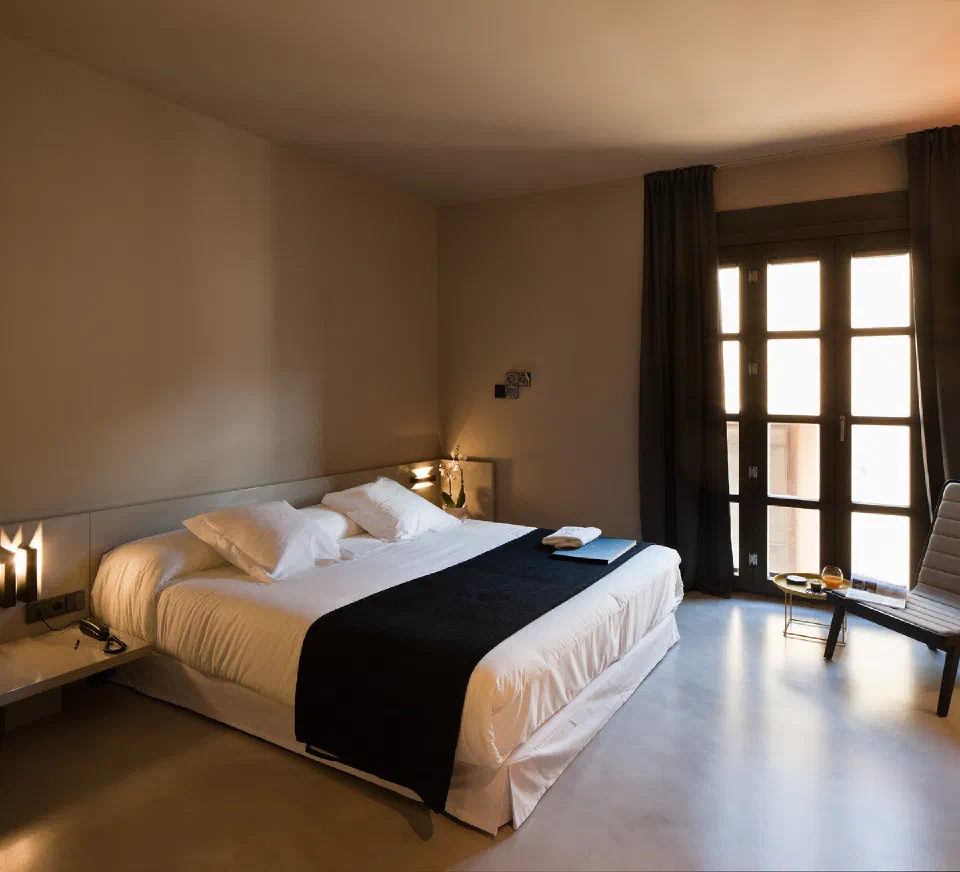 A double bed with a black runner and tall window at Caro Hotel.