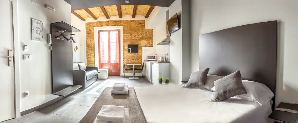 Bed, kitchenette and sofa beneath exposed brick and beams in a Soho Valencia Loft Studio.